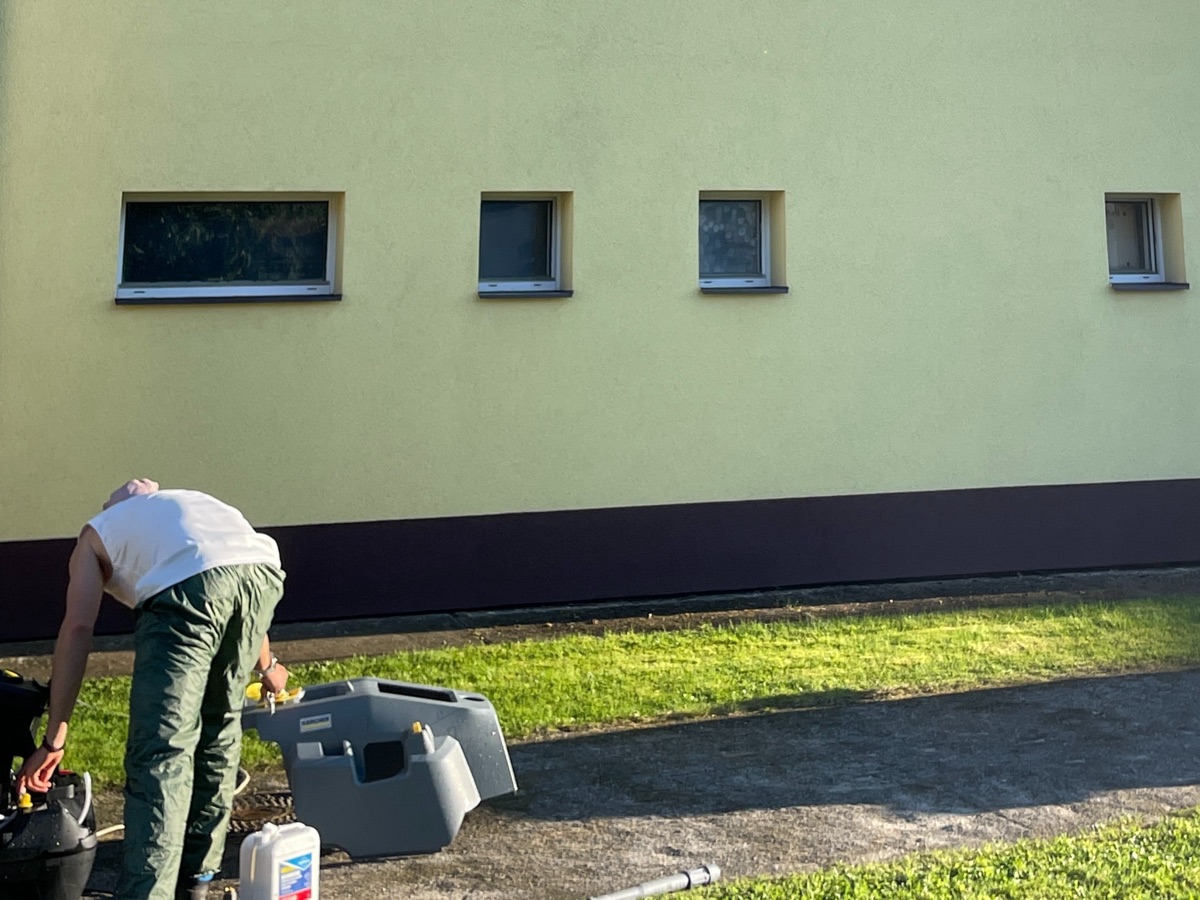 Tentýž panelový dům po vyčištění metodou Soft Wash — jednolitě čistá žlutá fasáda, technik připravuje techniku