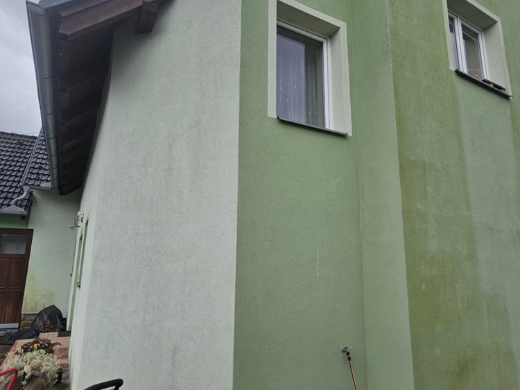 Rohový pohled na zelenou fasádu - vlevo světlejší ošetřená část, vpravo tmavší stěna ještě pokrytá řasovým povlakem