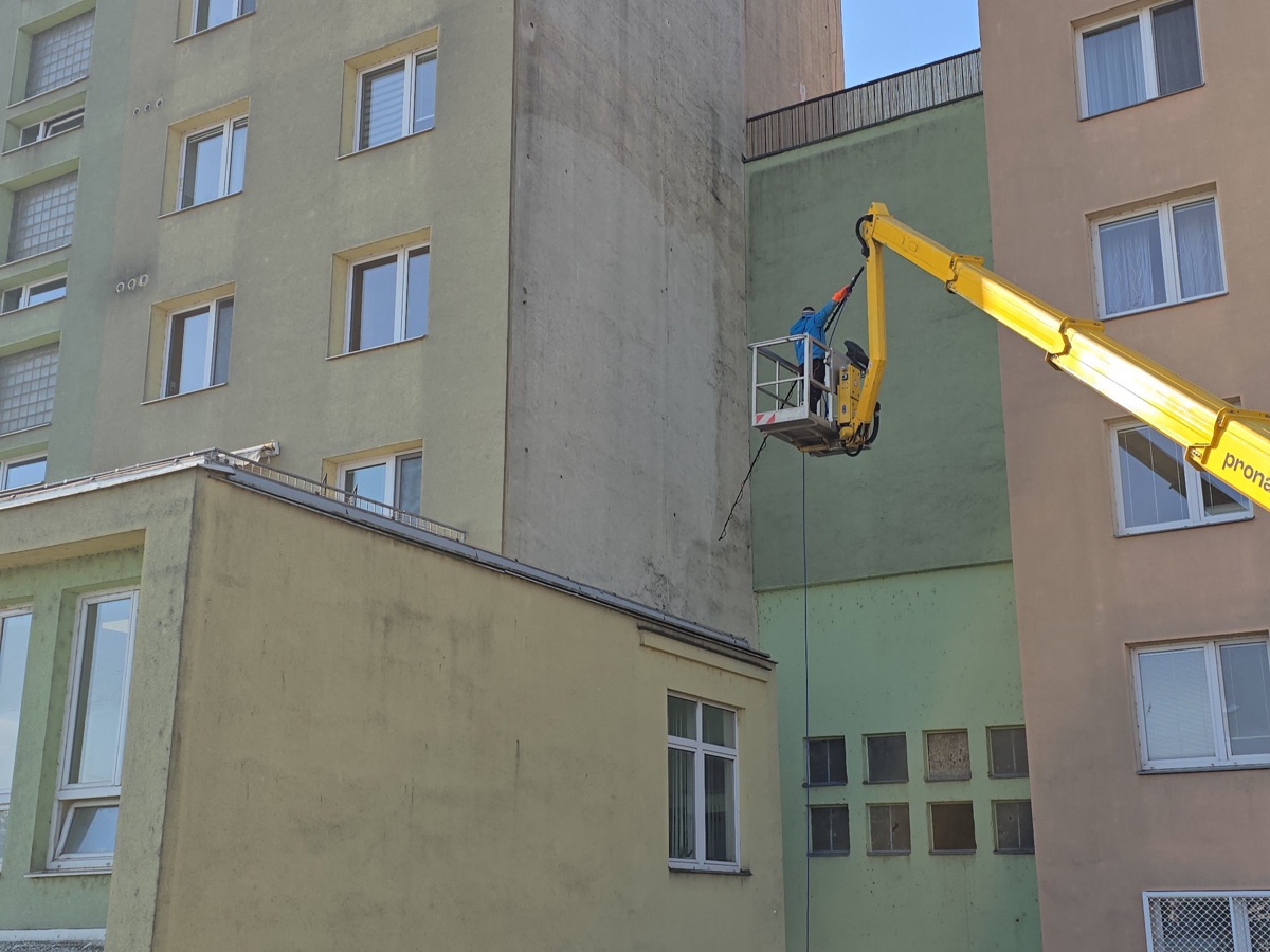 Technik na kloubové plošině čistí fasádu vysokého panelového bytového domu metodou Soft Wash