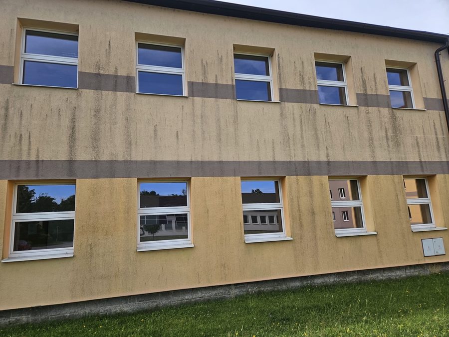 Omítka patrové budovy s výraznými tmavými svislými stružkami a plošným znečištěním pod okny