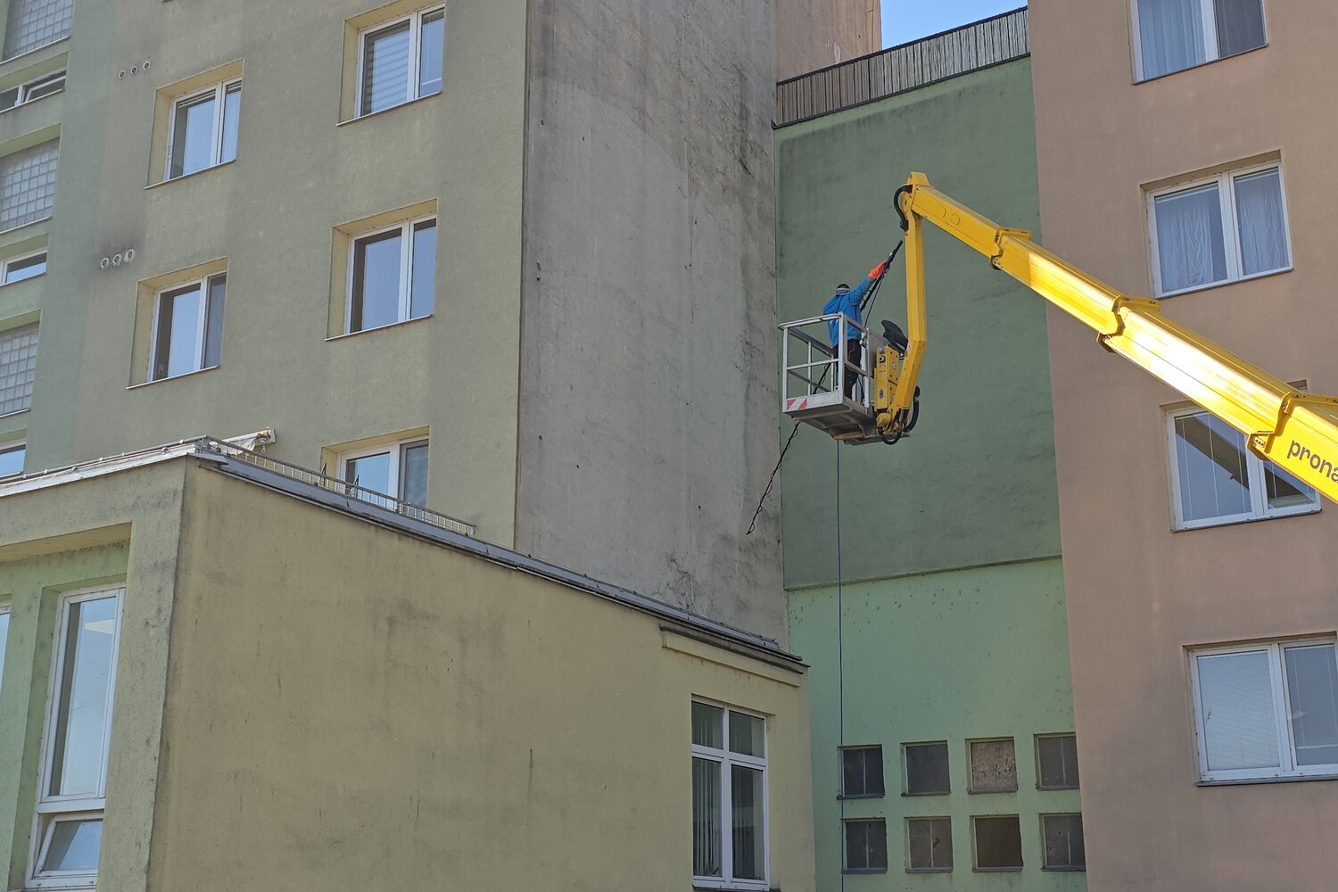Technik Elegantního Mytí čistí fasádu bytového domu z koše montážní plošiny - bez lešení