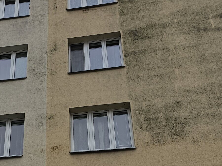 Bytový dům, na kterém je jedna část fasády výrazně tmavší než zbytek